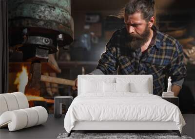 Real brutal blacksmith works in a workshop mechanical hammer with a red-hot iron. Portrait of a profession. Wall mural