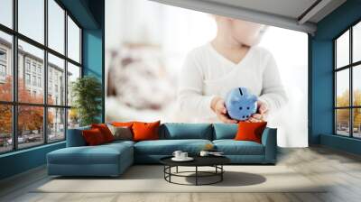 The child holds a blue money box in his hands. Savings for the future. Wall mural