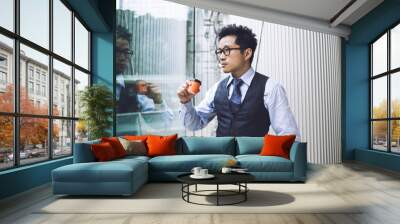 Asian man with coffee looking away Wall mural