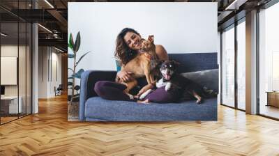 Joyful fit woman having fun with adorable mongrel dogs spending leisure time in home living room, cheerful female resting at comfortable couch with cute doggie pets enjoying friendship indoors Wall mural