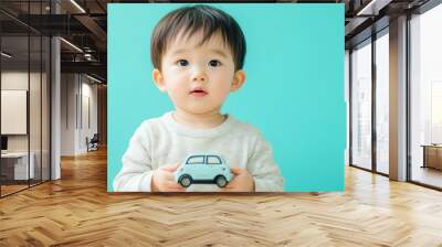 A baby boy in a white shirt looking at the camera while holding a toy car. Wall mural