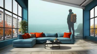 A man stands on a cliff overlooking the ocean in the fog. Wall mural