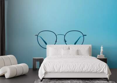 A pair of black framed round glasses on a blue background. Wall mural