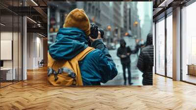 A photographer with a camera and backpack in a city street takes a picture. Wall mural