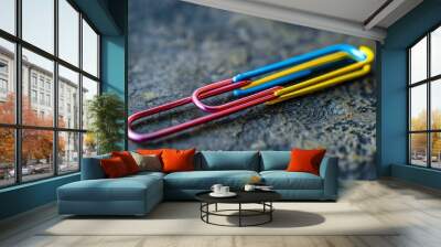 A red, yellow, and blue paperclip on a dark, textured surface. Wall mural