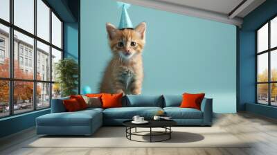 A small orange kitten with a blue party hat sits on a blue background with two toy balls. Wall mural