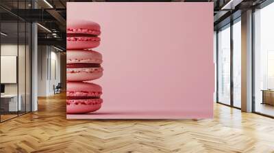 A stack of four macarons, two beige with white filling and two pink with brown filling, on a pink background. Wall mural