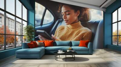 A young woman is sitting in the backseat of a car, looking at her phone. Wall mural