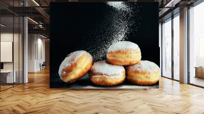 Powdered sugar is poured onto donuts. Traditional Jewish dessert Sufganiyot on black background. Cooking fried Berliners. Wall mural