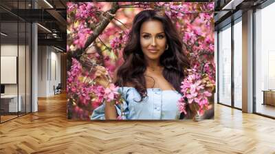 Beautiful brunette woman with taned skin posing near the blossom tree in the garden Wall mural