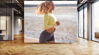 Beautiful young and healthy woman with blonde hair running alone on the beach near the sea Wall mural