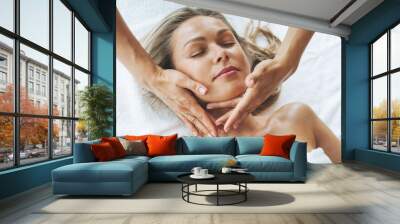 Attractive blonde young woman on couch with white linen enjoys hand facial massage in spa salon, treat yourself Wall mural