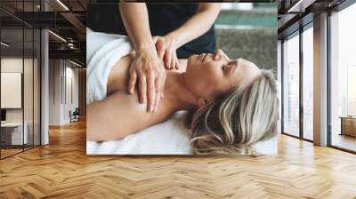 Attractive blonde young woman on couch with white linen enjoys hand facial massage in the spa salon, treat yourself Wall mural