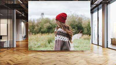 Beautiful carefree long hair asian girl in the red hat and knitted nordic sweater from behind in autumn nature park Wall mural