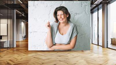 Beautiful happy emotional brunette young woman plus size body positive in comfortable sport wear near white brick wall Wall mural