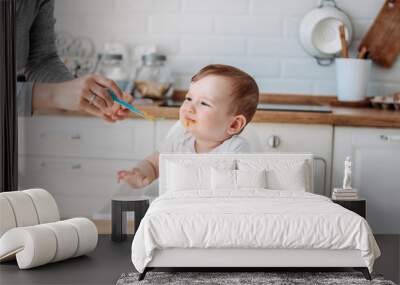 Charming little baby boy 6-8 months doesn't want to eat first food pumpkin from spoon with mom at home Wall mural