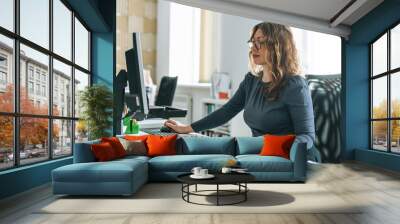 Charming smiling adult woman middle aged woman with curly hair architect designer working on computer in the bright modern office Wall mural