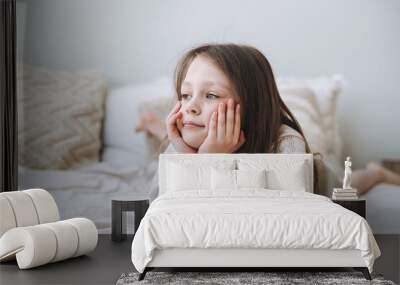 Cuty funny thinking little girl with long hair in home clothes having fun lies on bed at the home Wall mural