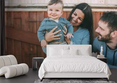 Happy family with cute baby boy on wooden house background outdoors, country life nature concept Wall mural