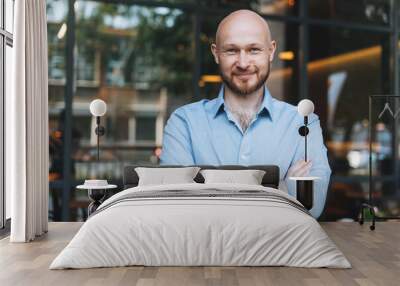 Portrait of Adult bald smiling attractive man forty years with beard in blue shirt businessman against glass wall of the street cafe Wall mural