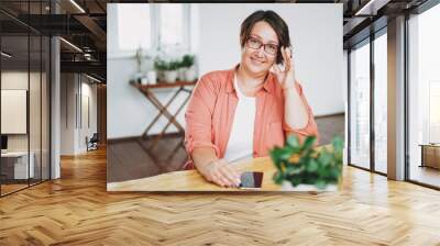 Portrait of adult charming brunette woman businesswoman in glasses plus size body positive using mobile at the home office Wall mural