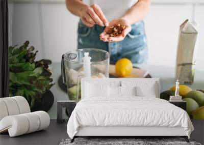 Young slim woman in white t-shirt and blue jeans cooking smoothie with bananas healthy food in kitchen at home Wall mural