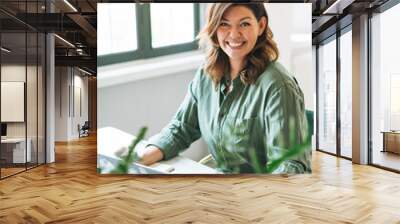 Young smiling brunette woman plus size working at laptop on table with house plant in bright modern office Wall mural