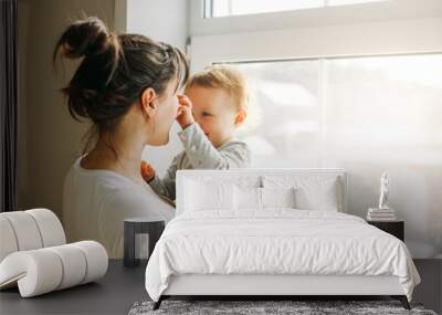 Young woman mom with baby girl on hands near window at home Wall mural