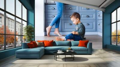 A cute little boy is sitting on the kitchen floor with his mother in the background Wall mural