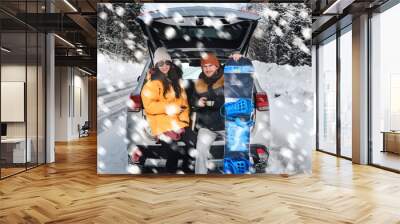 Smiling couple is sitting in the back trunk of suv car on roadside of winter road. Family trip to ski resort. light snack on the way. traveling lifestyle concept. Wall mural