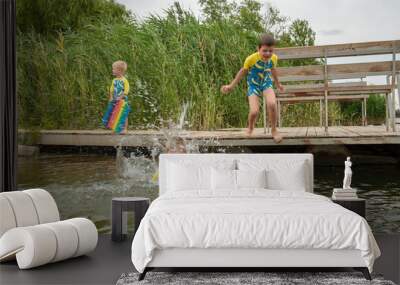 Funny children in swimsuits accelerate on wooden bridge near river and jump into water. boys are happy on holiday in village together. Summer day, river, swimming in water Wall mural