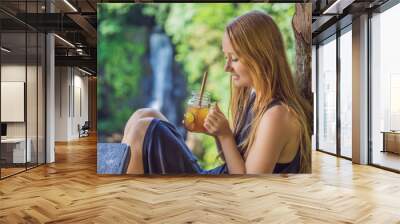 Closeup portrait image of a beautiful woman drinking ice tea with feeling happy in green nature and waterfall garden background Wall mural