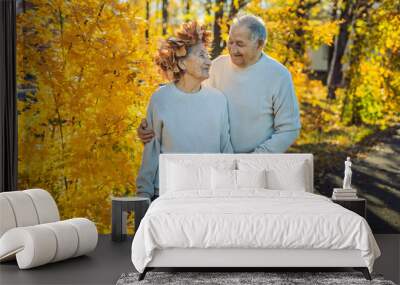 Happy old couple having fun at autumn park. Elderly man wearing a wreath of autumn leaves to his elderly wife Wall mural