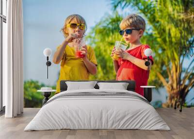 Two boys drink healthy smoothies against the backdrop of palm trees. Mango and watermelon smoothies. Healthy nutrition and vitamins for children Wall mural