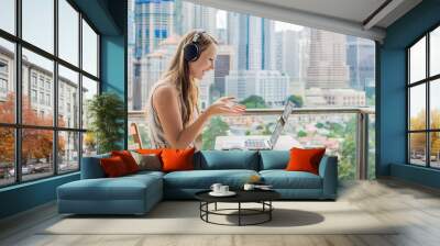 Young woman teaches a foreign language or learns a foreign language on the Internet on her balcony against the backdrop of a big city. Online language school lifestyle Wall mural