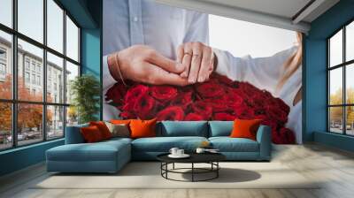 guy holds the girl's hand with a wedding ring over a bouquet of red roses Wall mural