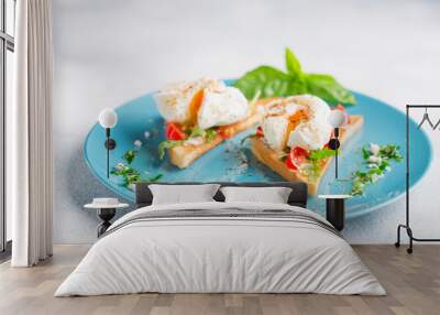 Two poached eggs on toasted toast with cherry tomatoes, cheese and herbs on a large blue plate Wall mural