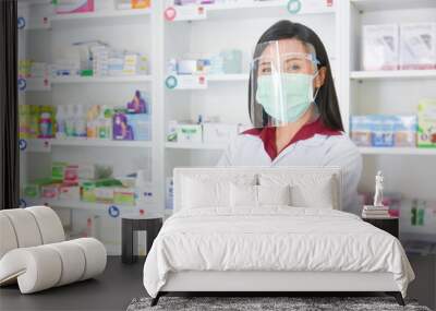 Asian professional young pharmacist wearing faceshield and mask while standing at drugstore. Wall mural