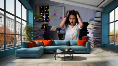 Stressed exhausted asian woman sitting at office desk and working overtime with overload work ducument on table. Wall mural