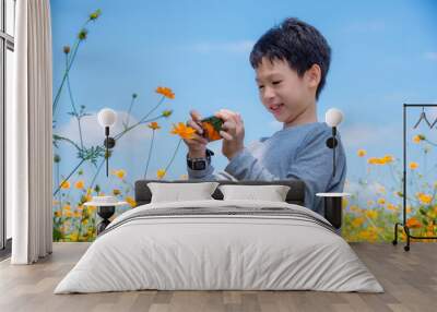 Young asian boy taking photo of flower by smart phone Wall mural