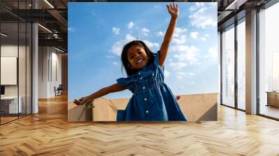 Cheerful little girl with arms outstretched in front of blue sky Wall mural