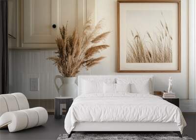 A close-up shot of the kitchen countertop with a framed print on the wall, dried grass in a white vase, and two jars placed beside it. The frame is wooden with a simple design, complementing the beige Wall mural