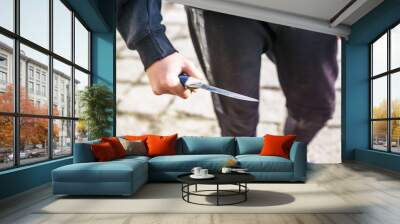 Close-up of a young man's hand with a knife, a big blade. Arrogance and violence among young people. Shallow depth of focus. Wall mural