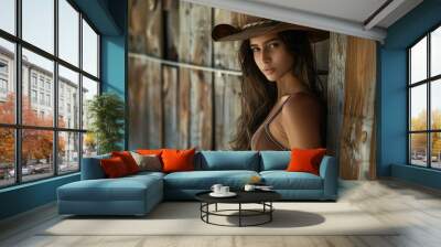 charming brunette woman in cowboy hat leaning against wooden wall Wall mural