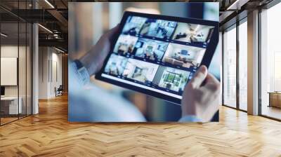 Close-up of person holding a tablet displaying security camera footage of different rooms Wall mural