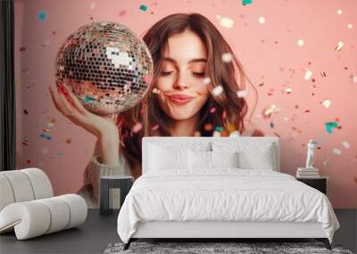 Happy woman holding a disco ball with confetti falling around on a vibrant pink background Wall mural