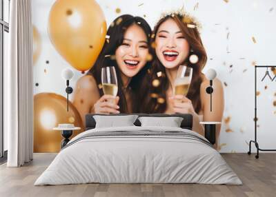 portrait of two attractive asian girls wearing elegant dress holding a glass of champagne, smilling with ballons and confetti on white background Wall mural