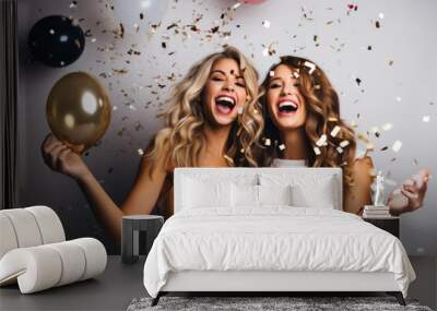 portrait of two attractive caucasian girls wearing elegant dress holding a glass of champagne, smilling with ballons and confetti on white background Wall mural