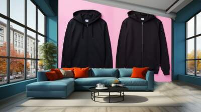 Two black zip up hoodies with hoods and pockets, neatly displayed against a contrasting pink background Wall mural