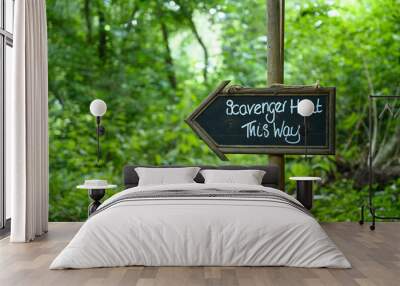 Scavenger hunt this way signpost in lush forest woodland Wall mural